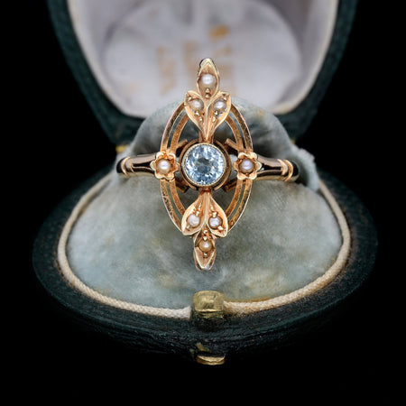 Antique Edwardian aquamarine ring in gold with a round-cut aquamarine centre stone surrounded by seed pearls in an ornate navette-shaped openwork setting, circa 1905