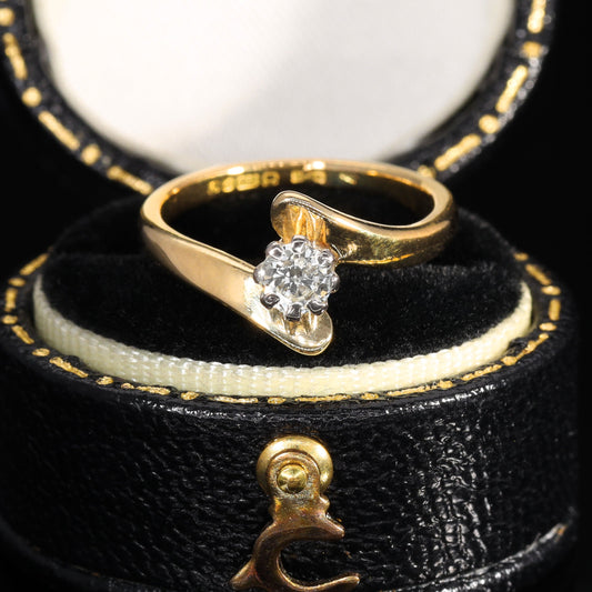 Vintage 1977 crossover solitaire ring in 18ct yellow gold with brilliant-cut diamond set in a white metal collet, showing the characteristic bypass shank