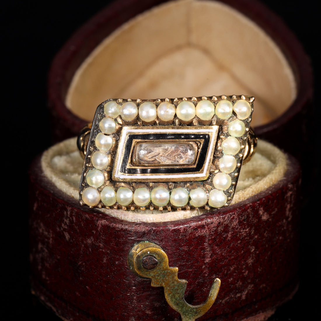 Georgian mourning ring with rectangular bezel displaying woven hairwork under crystal, bordered by black and white enamel and two rows of seed pearls, circa 1810
