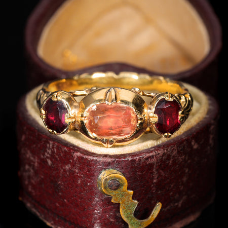 Antique French 19th-century three-stone ring with a central pinkish-peach topaz flanked by two deep red garnets in yellow gold, displayed in a period burgundy ring box