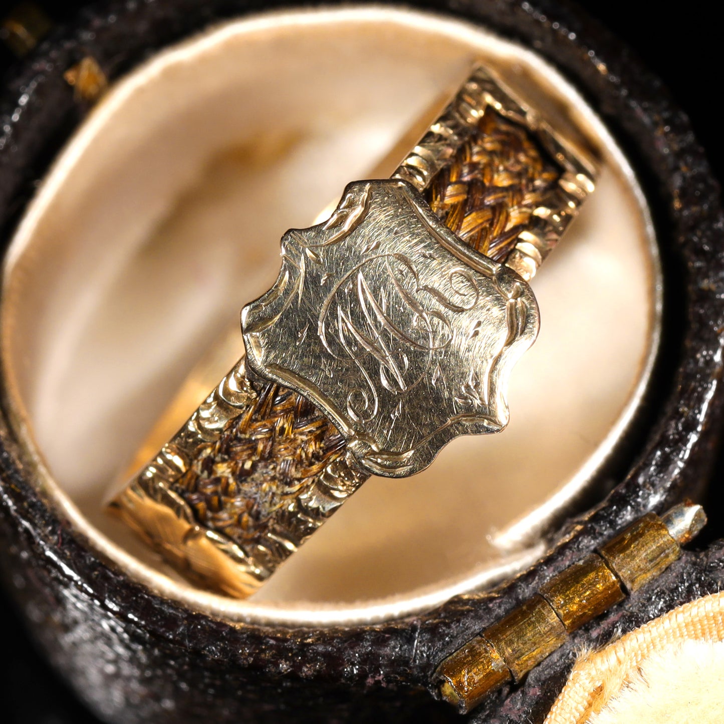 Close-up of engraved 'M.R' shield cartouche on braided hairwork band