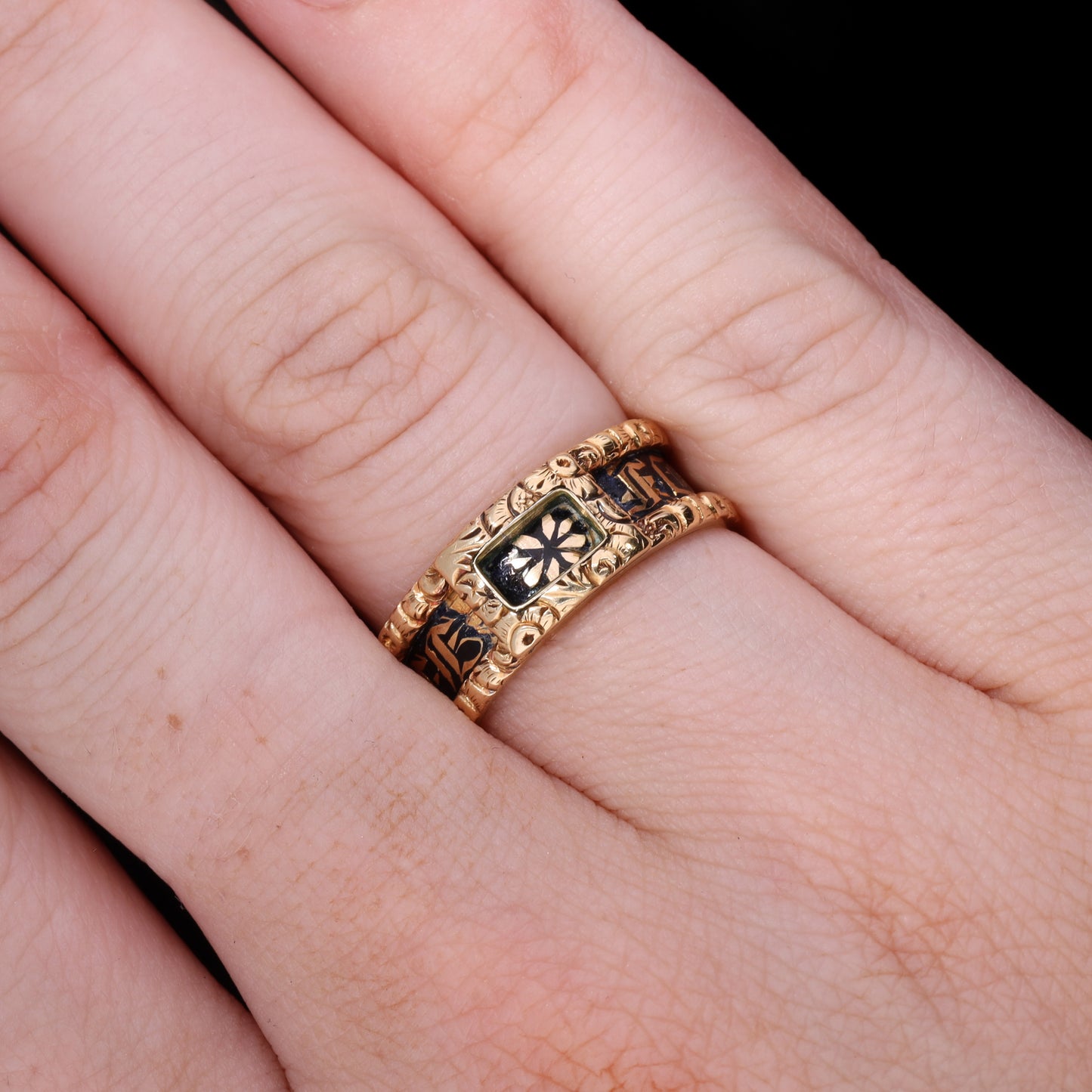 Ring worn on hand showing scale, black enamel and gold floral detail