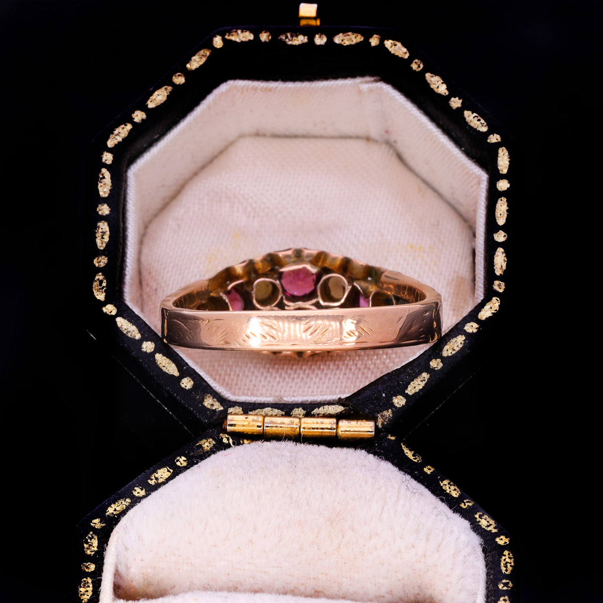 Side profile showing engraved band and open-back navette setting with garnet collets
