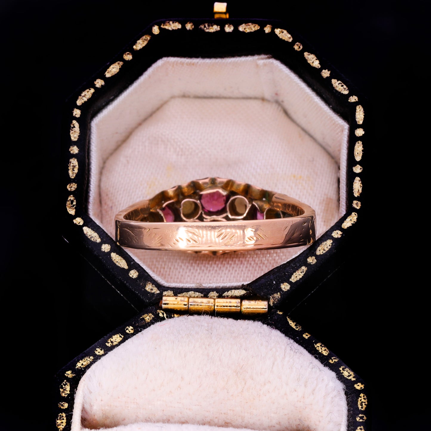 Side profile showing engraved band and open-back navette setting with garnet collets